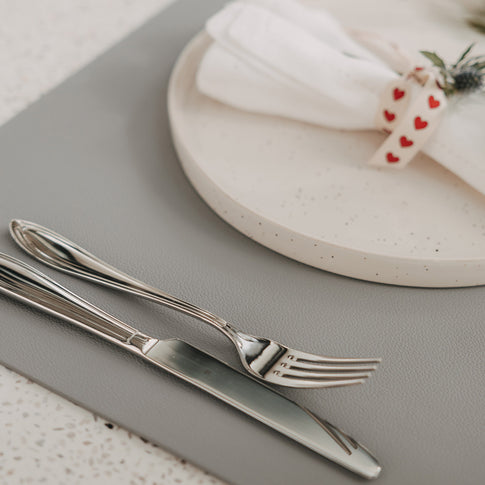 Graues Platzset in Lederoptik mit Teller, Serviette und Besteck auf gedecktem Tisch