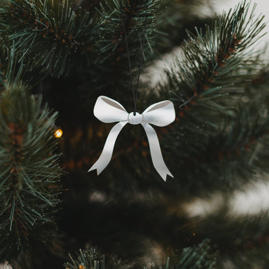Silberner Schleifenanhänger aus Metall am Weihnachtsbaum mit Lichterkette, stilvoll und festlich dekoriert.