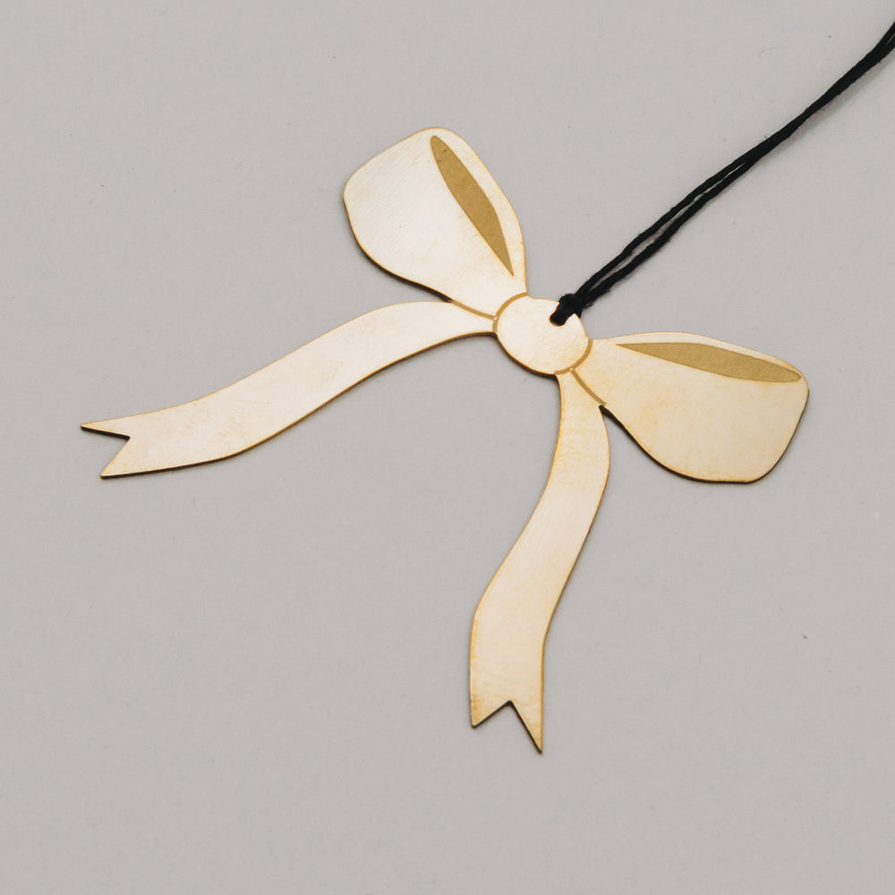 Detailaufnahme des goldenen Schleifenanhängers aus Metall mit feiner Struktur und schwarzem Band.