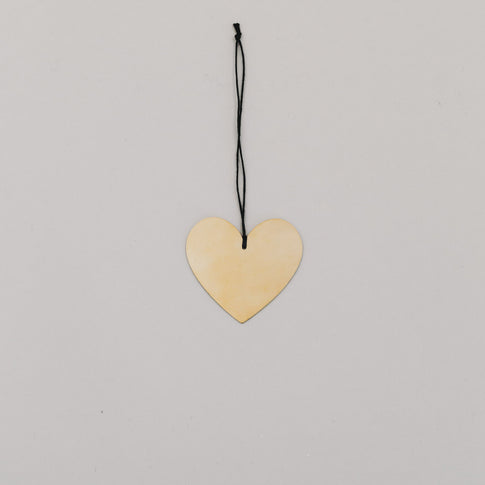 Herzförmiger goldener Metallanhänger mit schwarzem Band auf hellem Untergrund, flach ausgelegt.
