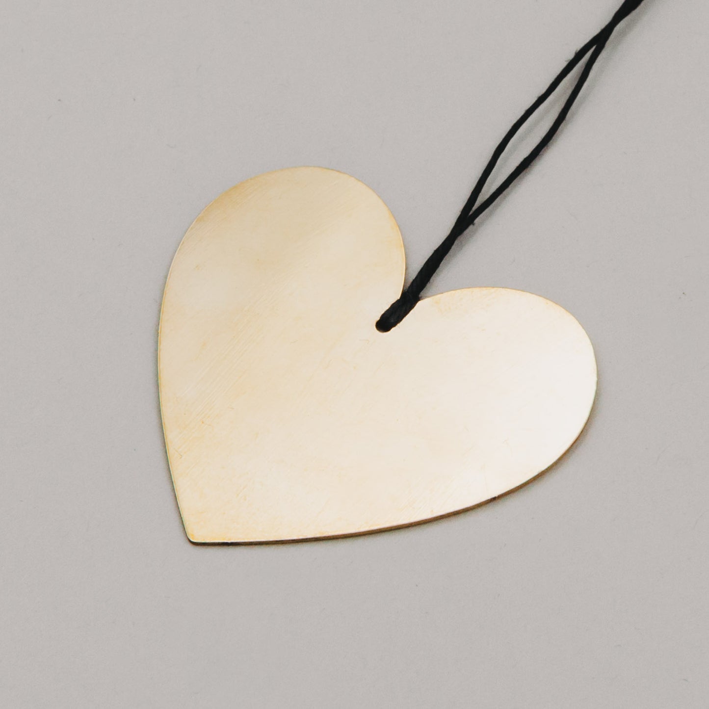 Nahaufnahme eines glänzenden Herzanhängers aus Goldmetall mit Aufhängeband in Schwarz auf grauem Hintergrund.