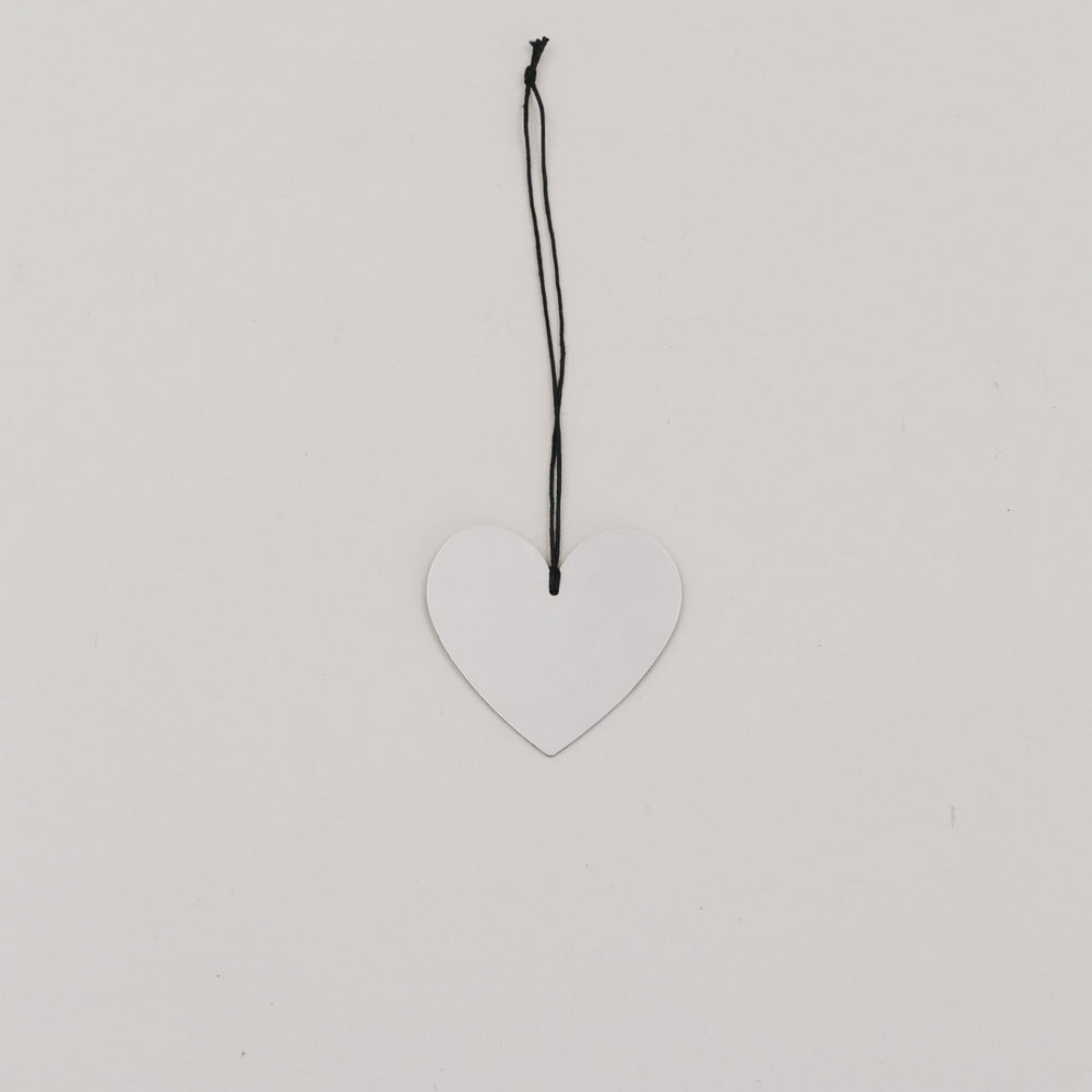 Metallanhänger in Herzform, silbern glänzend, mit schwarzer Kordel auf hellem Hintergrund