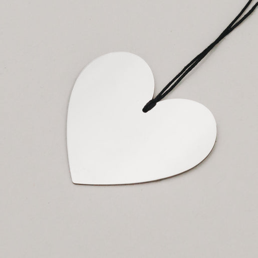 Detailaufnahme eines silbernen Herzanhängers aus Metall mit schwarzer Aufhängung