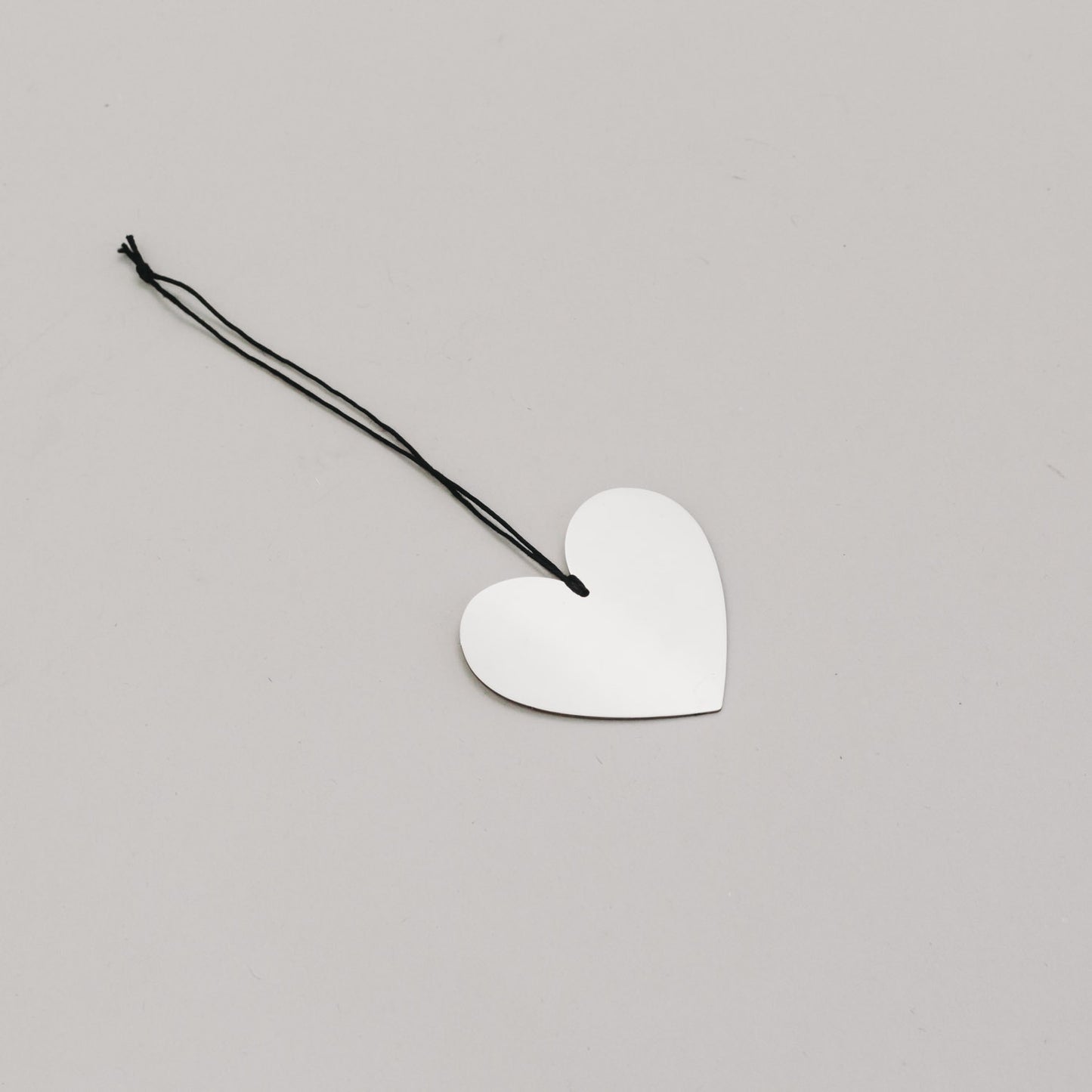 Silbernes Herz aus Metall mit schwarzem Band – flach auf hellem Untergrund fotografiert