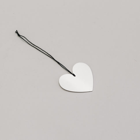 Silbernes Herz aus Metall mit schwarzem Band – flach auf hellem Untergrund fotografiert