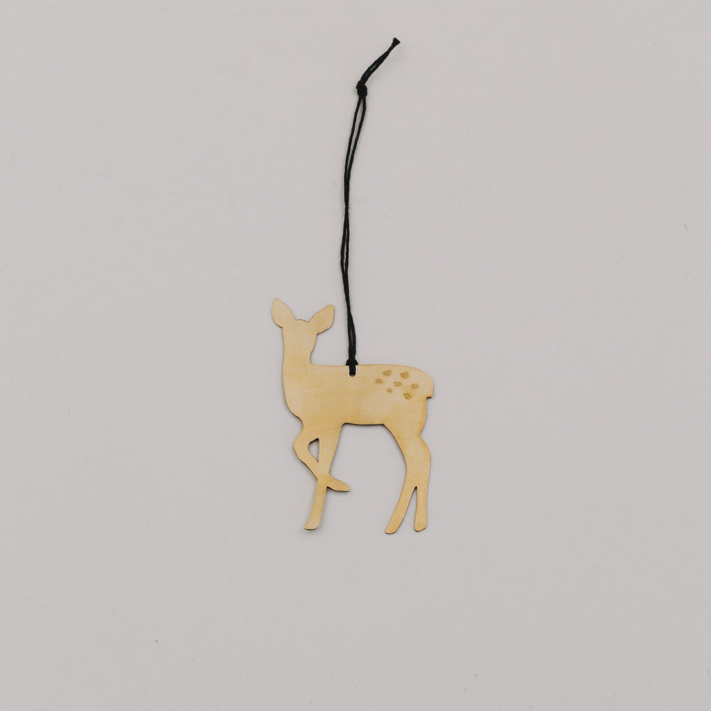 Goldener Rehnhänger aus Metall mit schwarzer Kordel auf hellem Hintergrund, minimalistisch arrangiert.