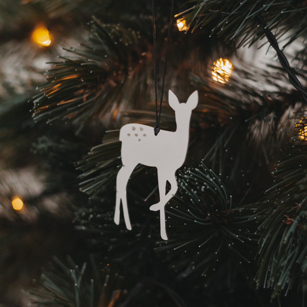 Silberner Rehanhänger  mit schwarzem Band an grünem Tannenzweig, umgeben von warmem Lichterglanz.