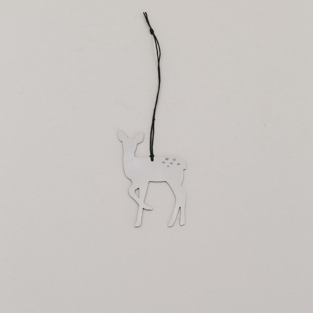 Silberner Rehnhänger aus Metall mit schwarzer Kordel auf hellem Hintergrund, minimalistisch arrangiert.