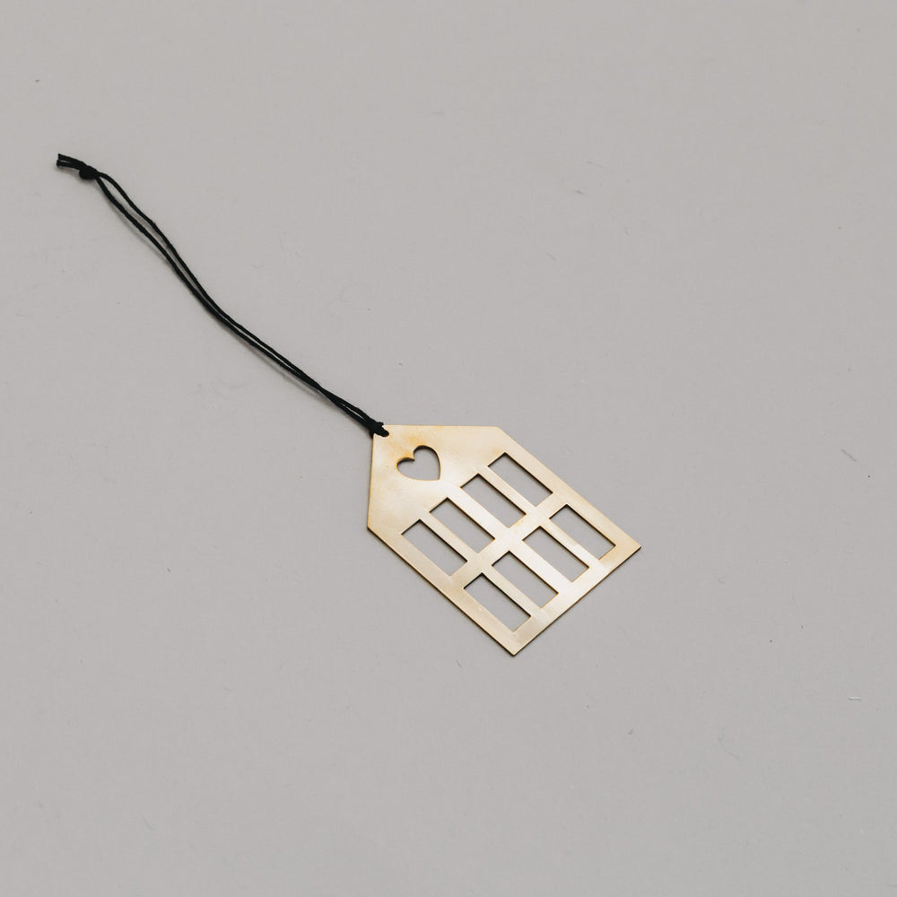 Schlichter goldener Hausanhänger aus Metall mit schwarzem Band, auf hellem Untergrund liegend.