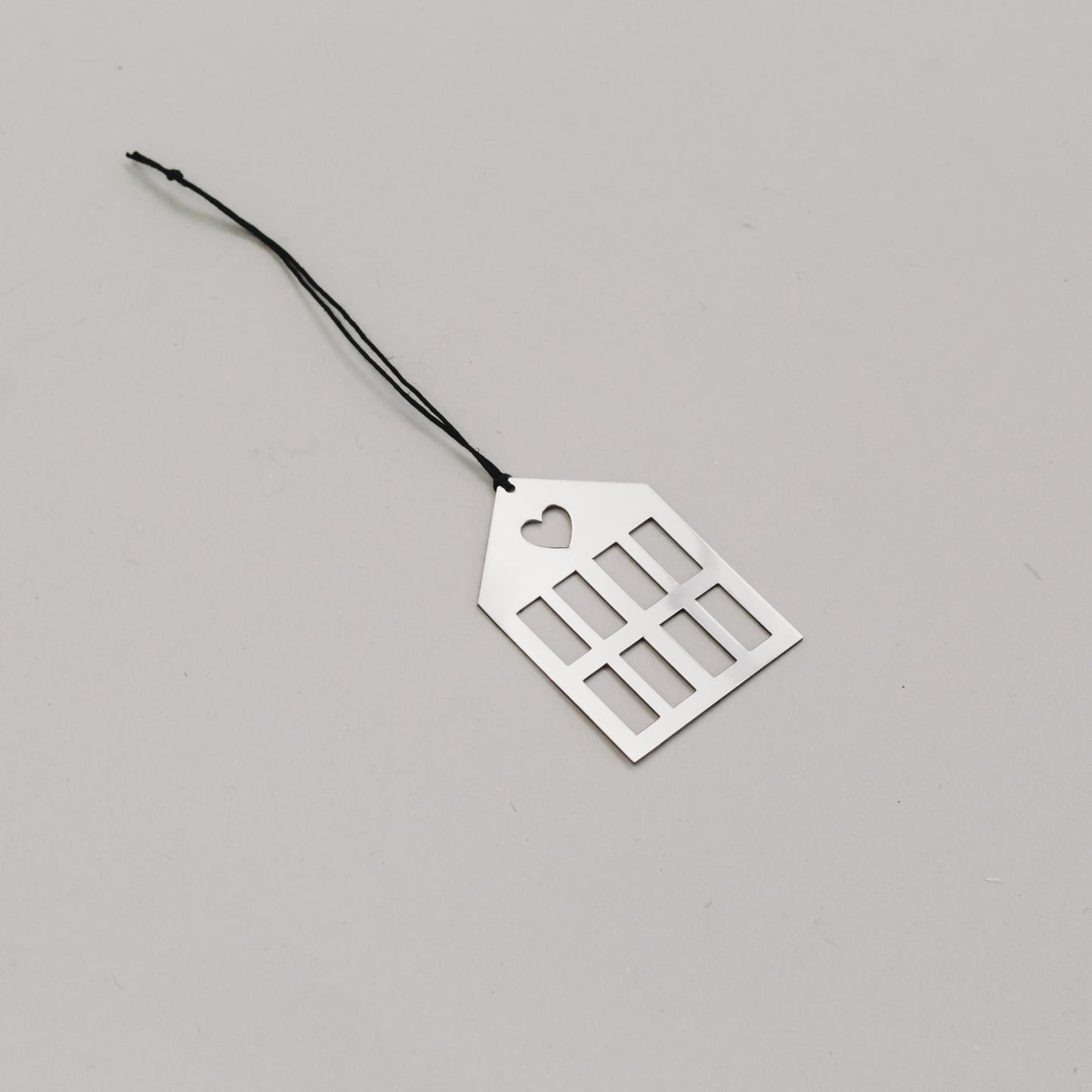 Schlichtersilberner Hausanhänger aus Metall mit schwarzem Band, auf hellem Untergrund liegend.