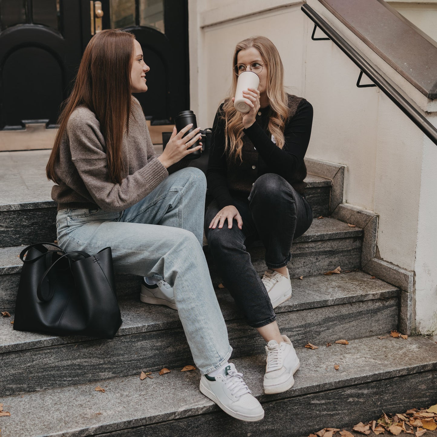 Zwei Frauen sitzen auf Treppe mit To-go Bechern Herz, stilvoll und nachhaltig unterwegs.