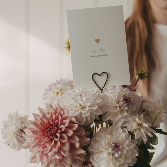 Schwarzer Herzstecker mit Grußkarte „Wie schön, dass es dich gibt!“ in einem Blumenstrauß