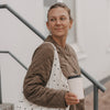 Frau mit cremefarbenem To-Go-Becher mit Herzmotiv und Stofftasche auf einer Treppe