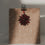 Schwarzer Herz-Clip befestigt einen roten Papierstern an einer weihnachtlichen Geschenktüte mit Tannenbaum-Muster.