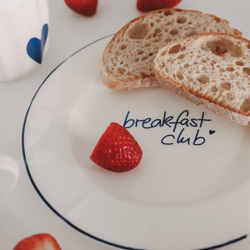 Frühstücksteller mit „breakfast club“ Schriftzug und feinem Rand in dunkelblau, kombiniert mit frischem Brot und Erdbeeren.