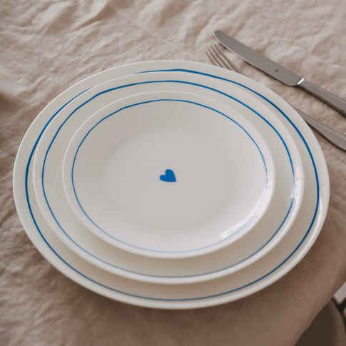 Drei gestapelte Porzellanteller in verschiedenen Größen mit hellblauem Rand und Herzdetail auf gedecktem Tisch.