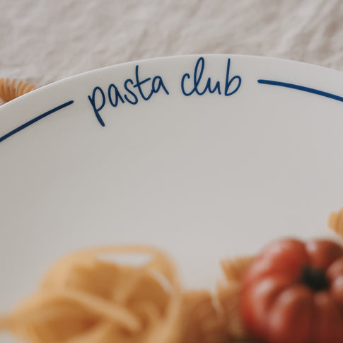 Detailaufnahme des Schriftzugs „pasta club“ auf einem weißen Teller mit dunkelblauem Rand.
