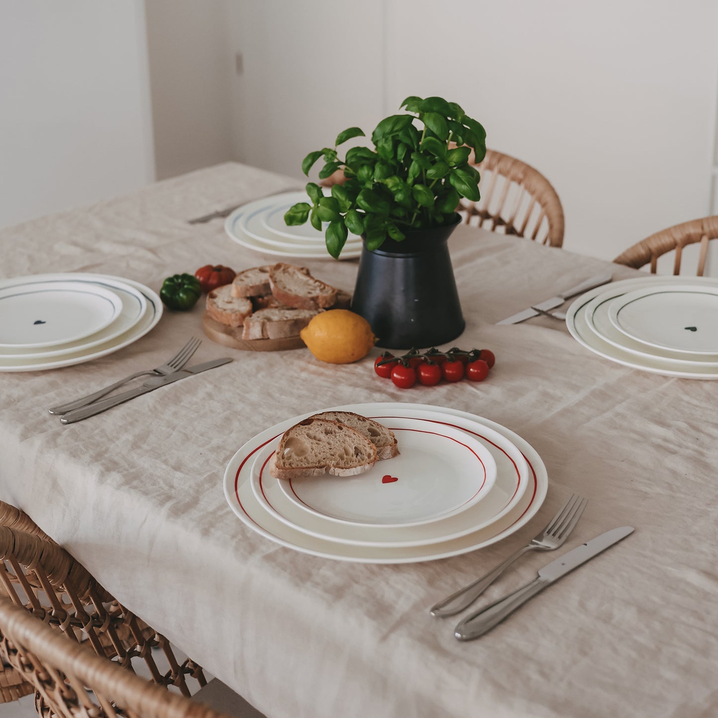 Esstisch mit weißen Tellern mit rotem Rand und kleinem Herz, dekoriert mit Brot, Zitronen und Cherrytomaten.