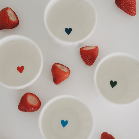 Herzbecher mit Getränk von oben, umgeben von frischen Erdbeeren, stilvolle Keramik Tasse