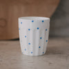 Weißer Porzellanbecher mit kleinen blauen Herzen auf Tisch, minimalistisches Design