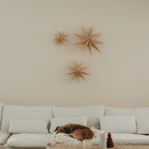 Drei braune Papiersterne mit Lichterkette als natürliche Weihnachtsdeko über einem weißen Sofa