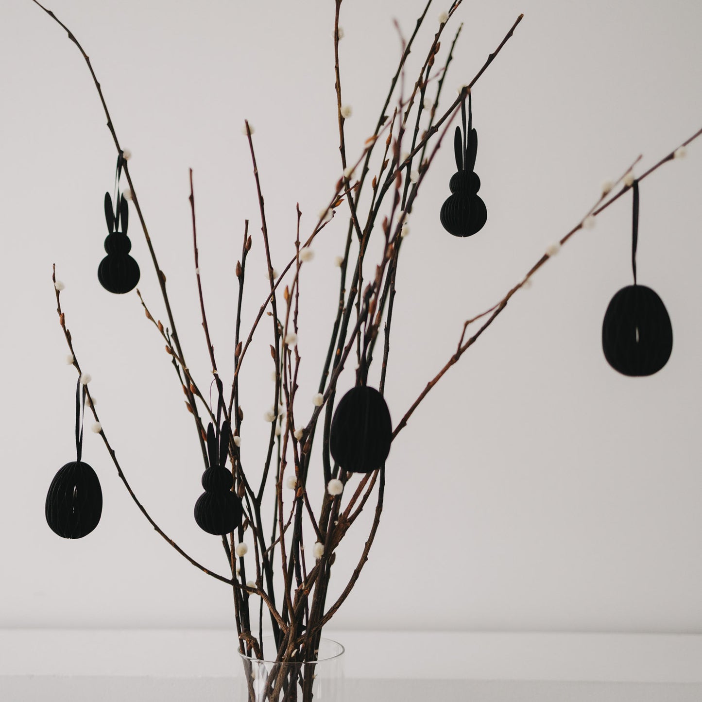 Schwarze Papier-Osteranhänger in Eiform und Hasenform an dekorierten Zweigen.