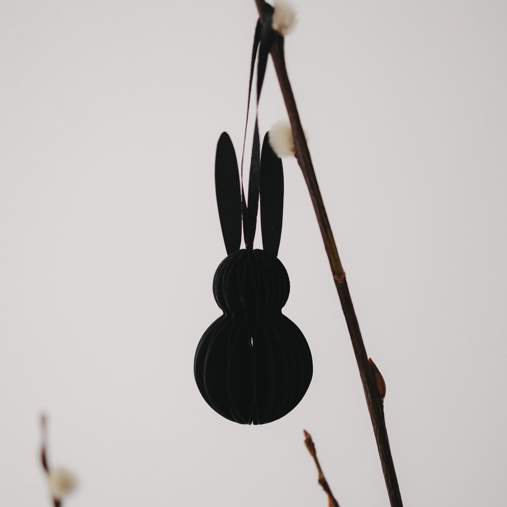Schwarzer Papieranhänger in Hasenform, hängend an einem Zweig in Nahaufnahme.