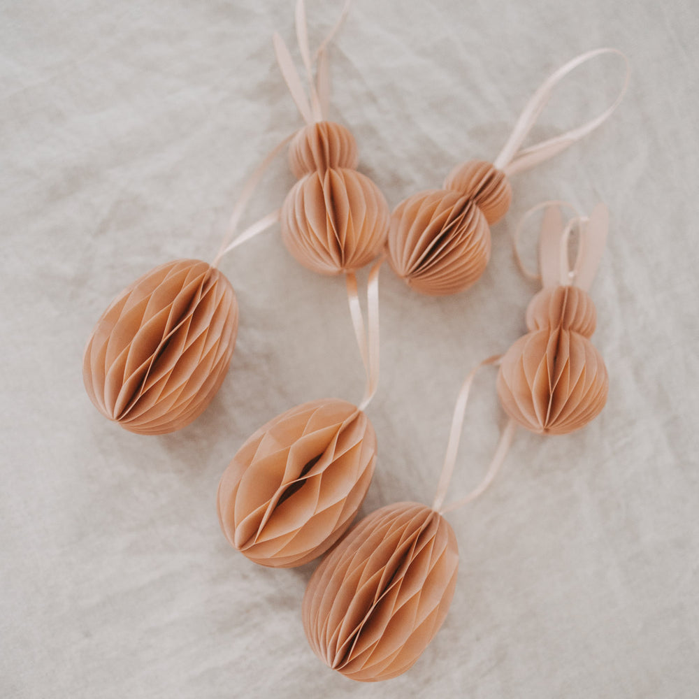 Peachfarbene Papieranhänger in Ei- und Hasenform als Osterdeko auf hellem Stoff.