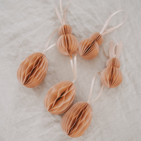Peachfarbene Papieranhänger in Ei- und Hasenform als Osterdeko auf hellem Stoff.