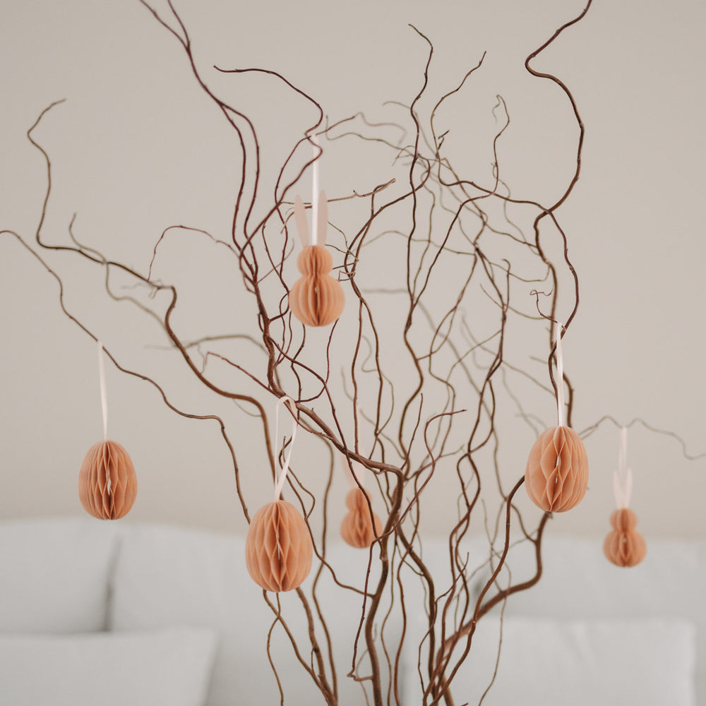 Peachfarbene Papieranhänger in Ei- und Hasenform hängen an dekorativen Zweigen.