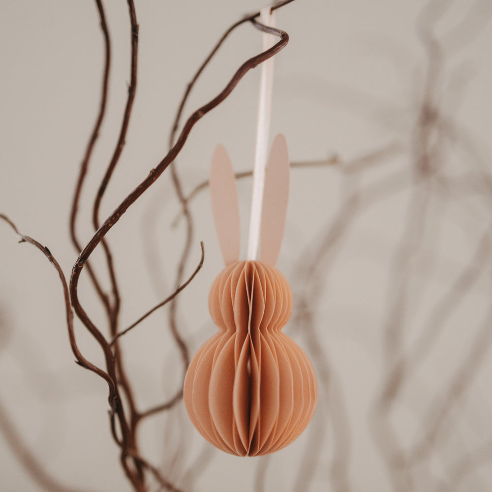 Nahaufnahme eines peachfarbenen Papieranhängers in Hasenform am Osterzweig.