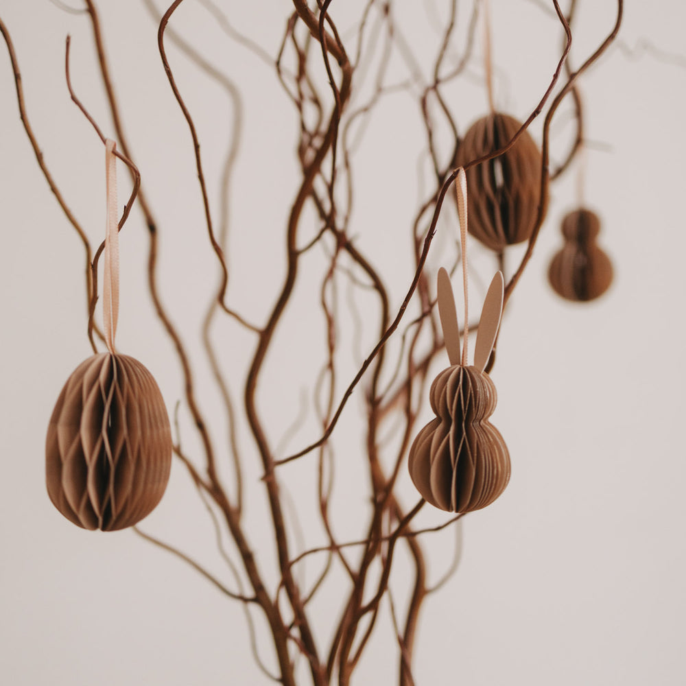 Natürliche Papieranhänger in Ei- und Hasenform hängen an gedrehten Zweigen.