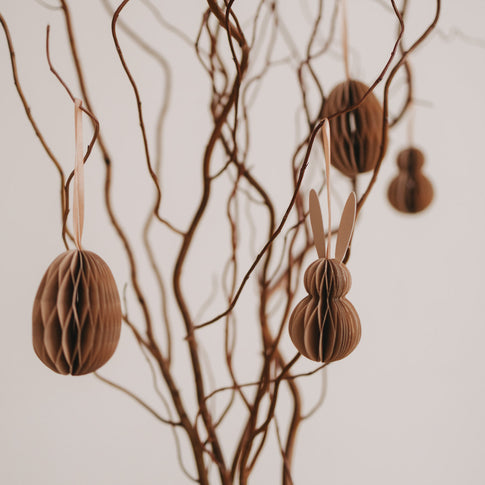 Natürliche Papieranhänger in Ei- und Hasenform hängen an gedrehten Zweigen.