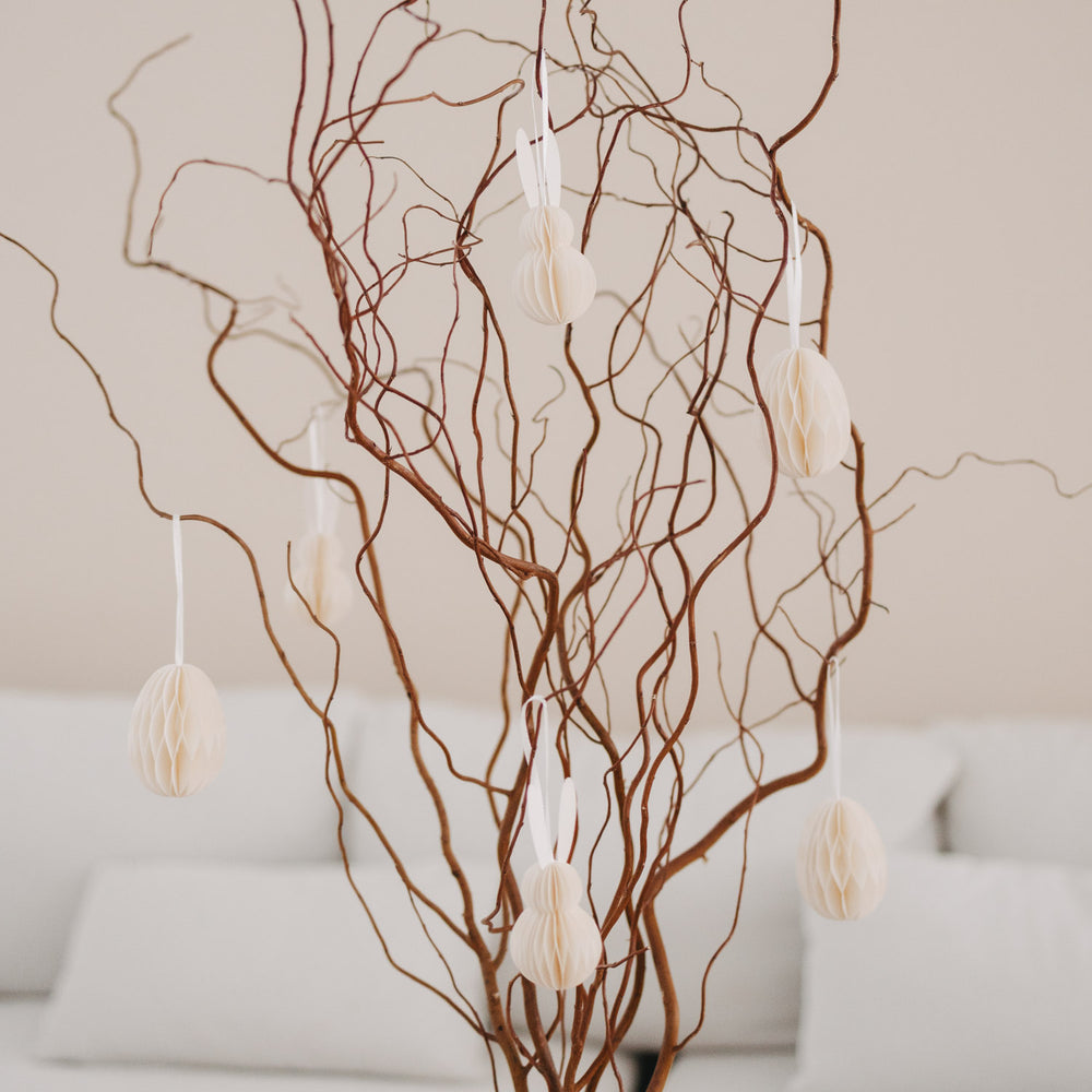 Beige Papieranhänger in Ei- und Hasenform an dekorativen Zweigen im Wohnzimmer.