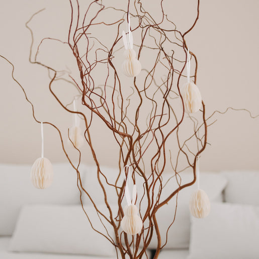 Beige Papieranhänger in Ei- und Hasenform an dekorativen Zweigen im Wohnzimmer.