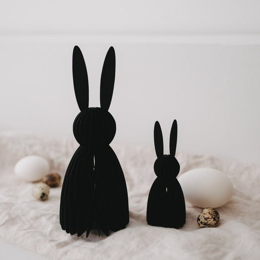 Schwarze Papierhasen im 2er-Set als Deko, arrangiert mit Eiern und Frühlingselementen auf Stoff.