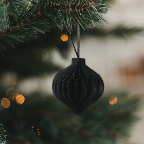 Schwarzer Papieranhänger in Kugelform am Weihnachtsbaum mit warmen Lichtern