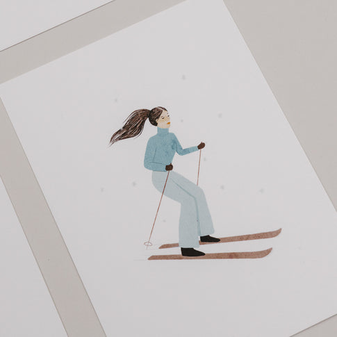 Weihnachtskarte mit einer Frau auf Skiern in blauer Winterkleidung vor weißem Hintergrund