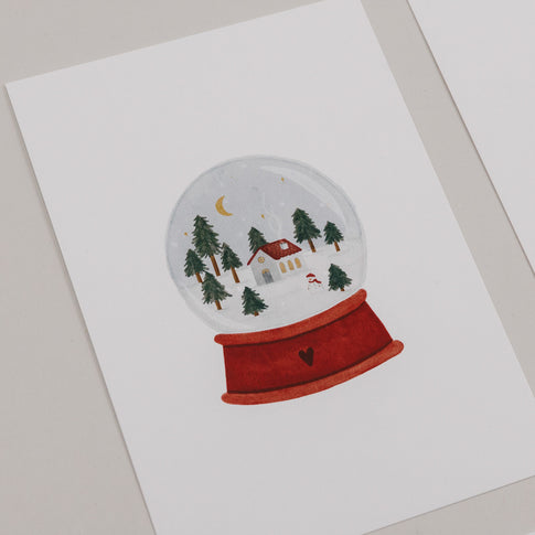 Weihnachtskarte mit Schneekugel, Häuschen, Bäumen und Mond auf rotem Sockel