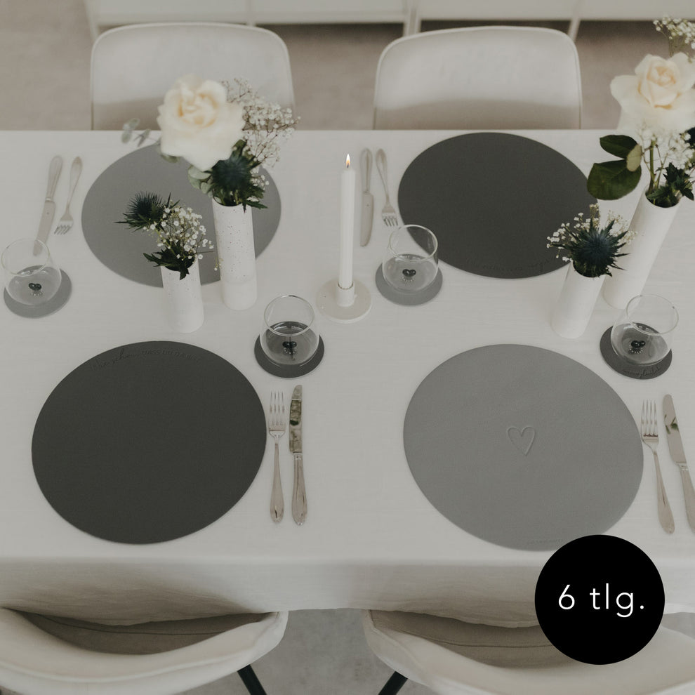 Gesamtansicht eines gedeckten Tisches mit grauen Platzsets und weißen Blumenvasen.