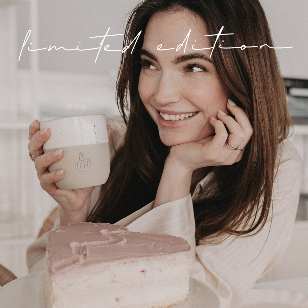 Frau mit Limited Edition Keramikbecher sitzt vor einem herzförmigen Kuchen und lächelt.