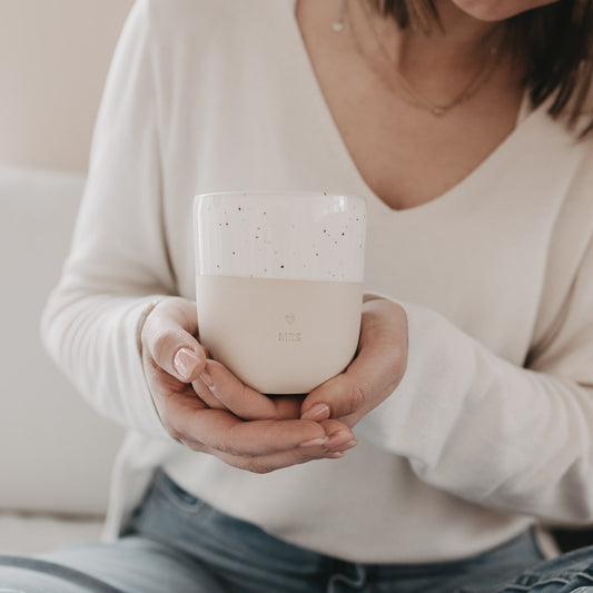 Frau hält MRS Keramikbecher aus Beige und Weiß im gemütlichen Setting.