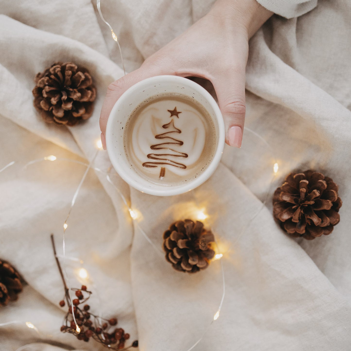 Blick in den Becher „O Tannenbaum“ mit Latte Art in Form eines Weihnachtsbaums, dekoriert mit Zapfen und Lichtern.