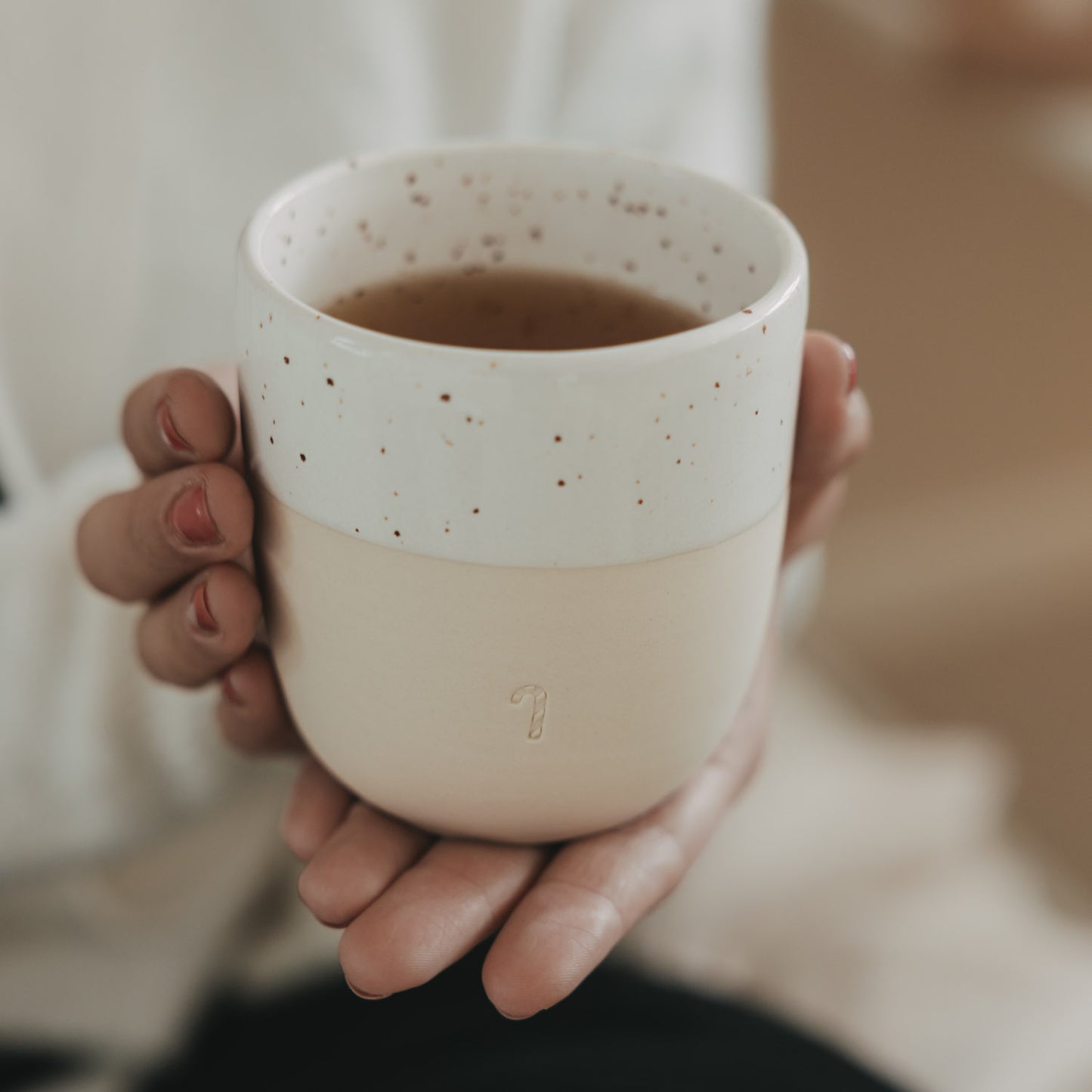 Hand hält Keramikbecher mit Zuckerstangen-Prägung, gefüllt mit Tee, schlichtes Design in warmem Licht