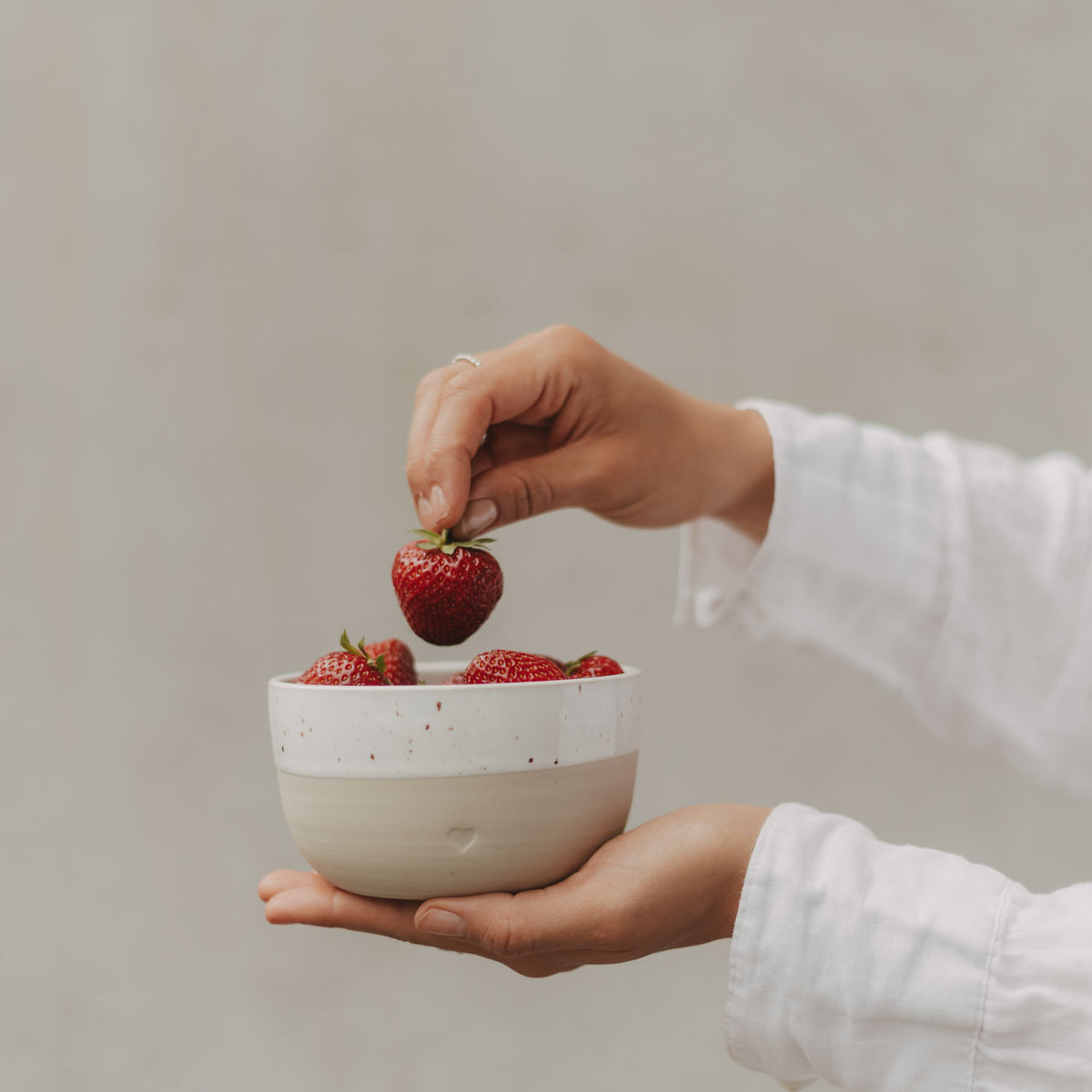 Beige-weiße Keramikschale mit Herz und frischen Erdbeeren, in den Händen gehalten