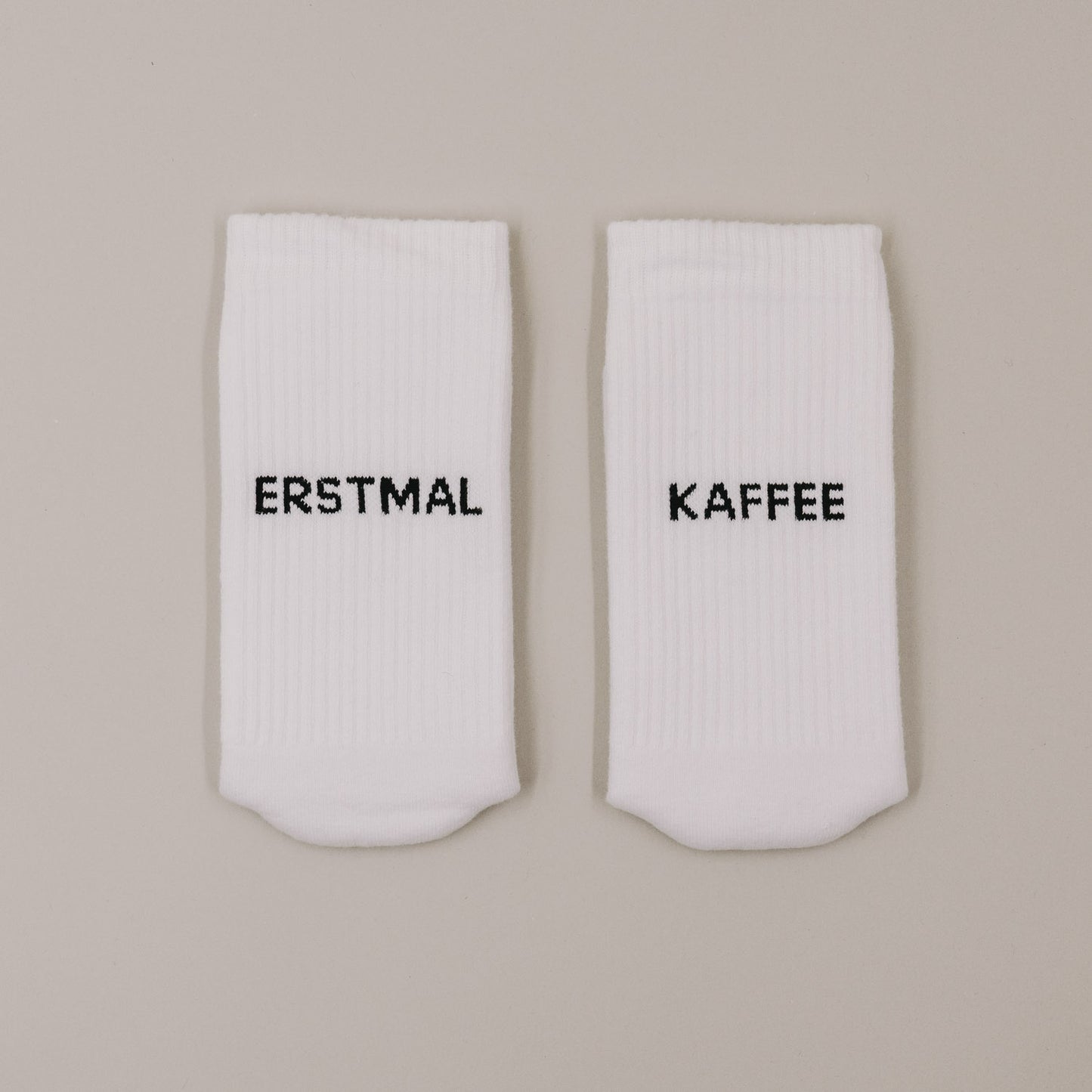 Flachliegende weiße Socken mit „Erstmal Kaffee“ Schriftzug minimalistisch