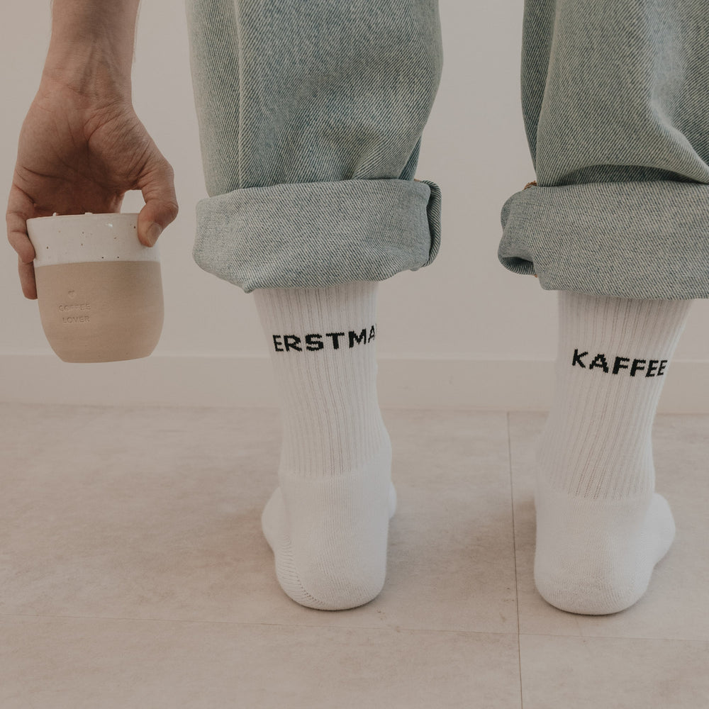 Detailansicht weißer Socken „Erstmal Kaffee“ mit hochgekrempelter Jeans