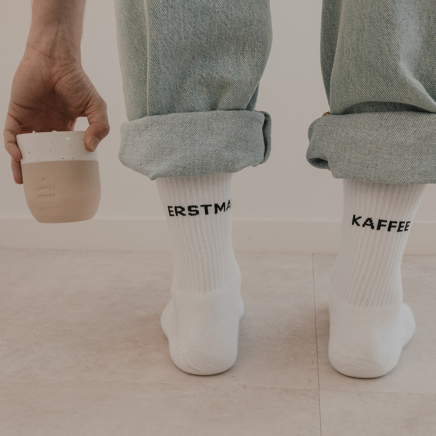 Detailansicht weißer Socken „Erstmal Kaffee“ mit hochgekrempelter Jeans