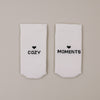 Flachliegende weiße Socken „Cozy Moments“ mit Herzsymbol und Schriftzug minimalistisch präsentiert