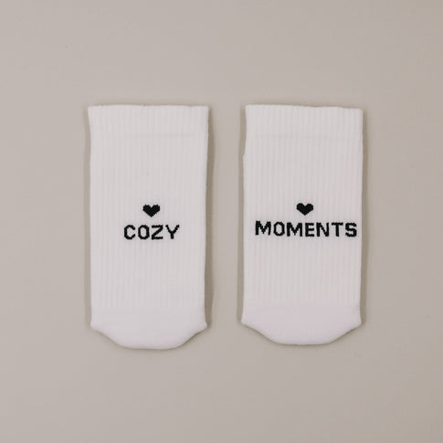 Flachliegende weiße Socken „Cozy Moments“ mit Herzsymbol und Schriftzug minimalistisch präsentiert
